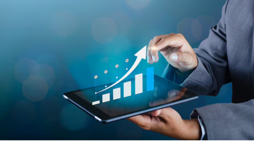 A person in a suit holds a tablet displaying a virtual bar graph with an upward arrow, symbolizing business growth and success on a blue, blurred background.
